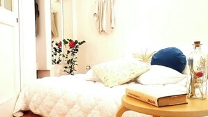 A bedroom with a white bed, a bedside table with a book, a vase with flowers, and a mirror on the wall. - La Piccina (Catania)