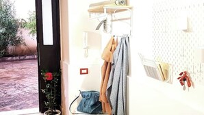 A room with a potted plant, a wooden bench, and a wall-mounted drying rack with towels and a handbag. - La Piccina (Catania)