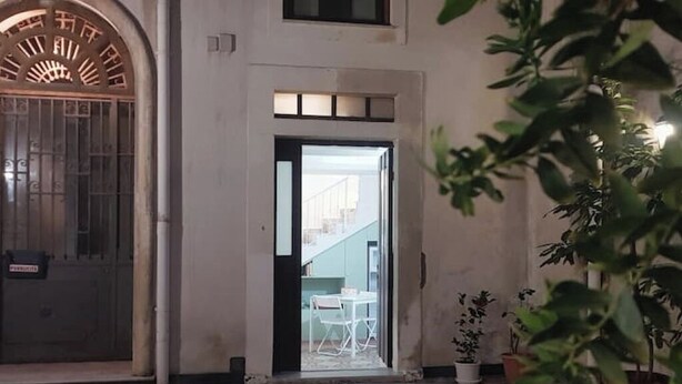 A doorway leading to a room with a table and chairs, surrounded by potted plants. - La Piccina (Catania)