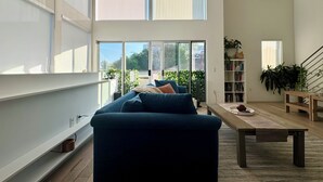 A modern living room with a sofa, a coffee table, and a bookshelf. There is a sliding glass door leading to an outdoor area. - Skydeck MidWilshire Modern Townhome with Garage, Rooftop Patio, and Loft Office (Los Angeles)
