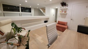 A modern living room with a sofa, a dining table, and a radiator. There is a staircase leading to an upper level. - Skydeck MidWilshire Modern Townhome with Garage, Rooftop Patio, and Loft Office (Los Angeles)