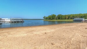 A sandy beach with a dock and a building on the water. - The Rustic Minnow: Walk to Lake, Enjoy Outdoor Amenities and Stunning Landscape  (Hulbert)