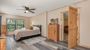 A bedroom with a bed, wooden dresser, and a closet with a wooden door. - The Rustic Minnow: Walk to Lake, Enjoy Outdoor Amenities and Stunning Landscape  (Hulbert)