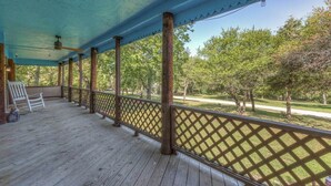 A covered porch with wooden flooring and a lattice railing, overlooking a grassy area with trees. - The Rustic Minnow: Walk to Lake, Enjoy Outdoor Amenities and Stunning Landscape  (Hulbert)