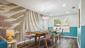 Uma sala de jantar com mesa de madeira, cadeiras cor-de-rosa e um lustre.