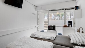 Ein Schlafzimmer mit Bett, Schreibtisch mit Computer, Kaffeemaschine und Fenster mit Blick auf Bäume.