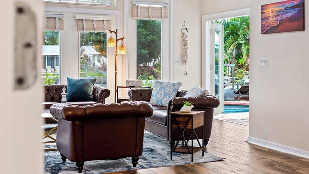 A spacious living room with leather sofas, a wooden coffee table, and a view of a swimming pool.