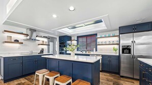 A modern kitchen with dark blue cabinets, a stainless steel refrigerator, and a central island with stools.