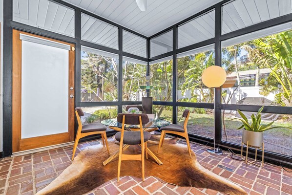 Una habitación con puerta de vidrio, una mesa redonda con sillas, un tapete de cuero de vaca y vista a la vegetación exterior.