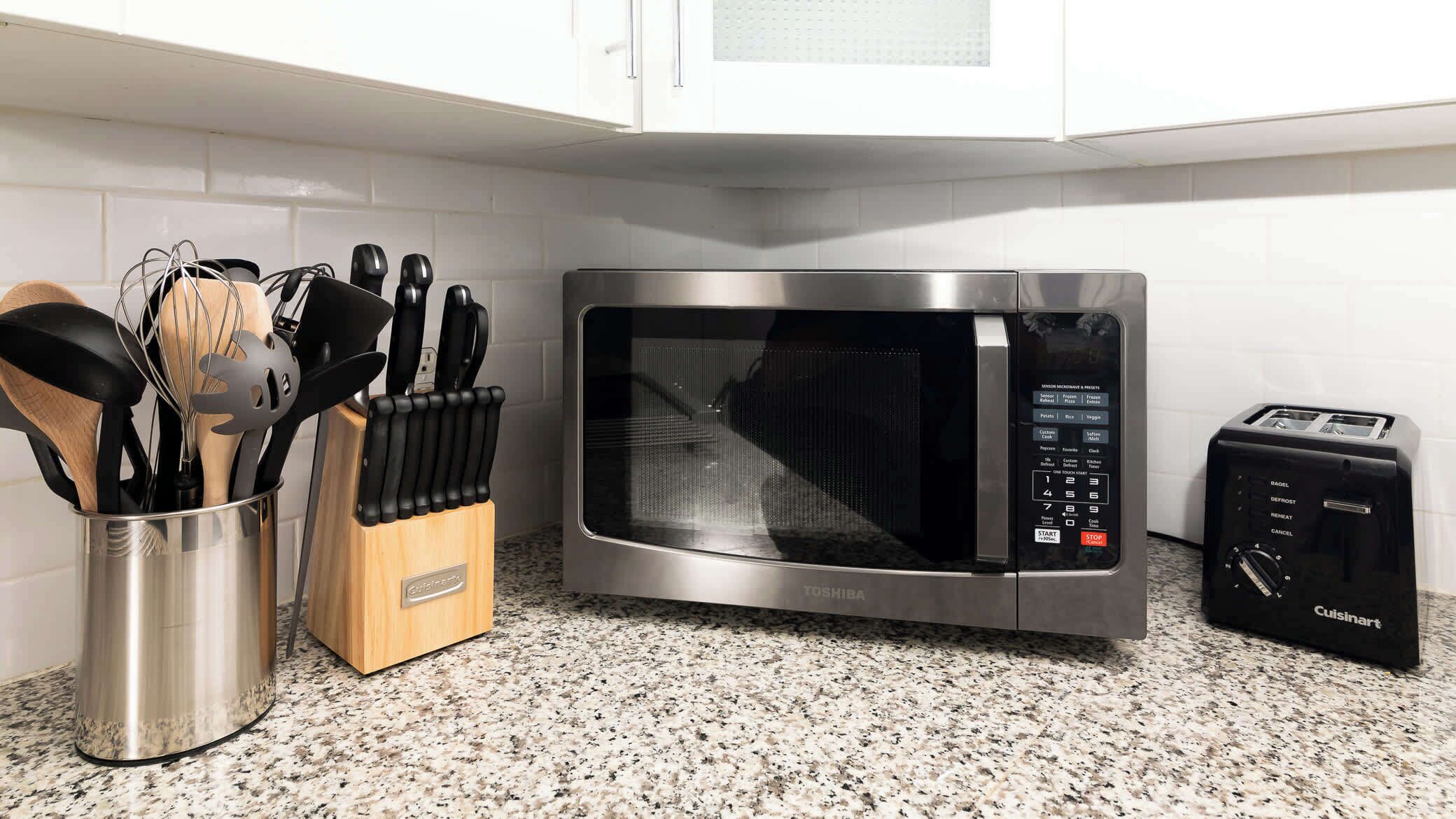 Een keuken met een roestvrijstalen magnetron, een broodrooster en een messenblok.