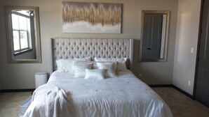 A bedroom with a tufted headboard, white bedding, and a large abstract painting above the bed. - 4-bedroom house in charming Coeur d'Alene with AC, WiFi, fitness room (Coeur d'Alene)