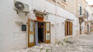 A building with a stone-paved street, a fan mounted on the wall, and a door with a curtain partially drawn. - Antica Casa 1600 by Rentbeat (Ostuni)