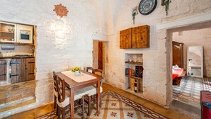 A rustic interior with exposed stone walls, a wooden dining table with chairs, a bookshelf, and a kitchen area with cabinets and a sink. - Antica Casa 1600 by Rentbeat (Ostuni)