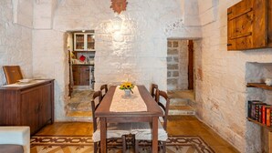 A stone-walled dining area with a table set for four, a wooden cabinet, and a bookshelf. - Antica Casa 1600 by Rentbeat (Ostuni)