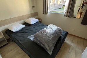 A single bed with a black mattress and white pillows, a wooden headboard, a small bedside table, and a window with curtains. - Louisiana, 6 people   (La Boissière-de-Montaigu)