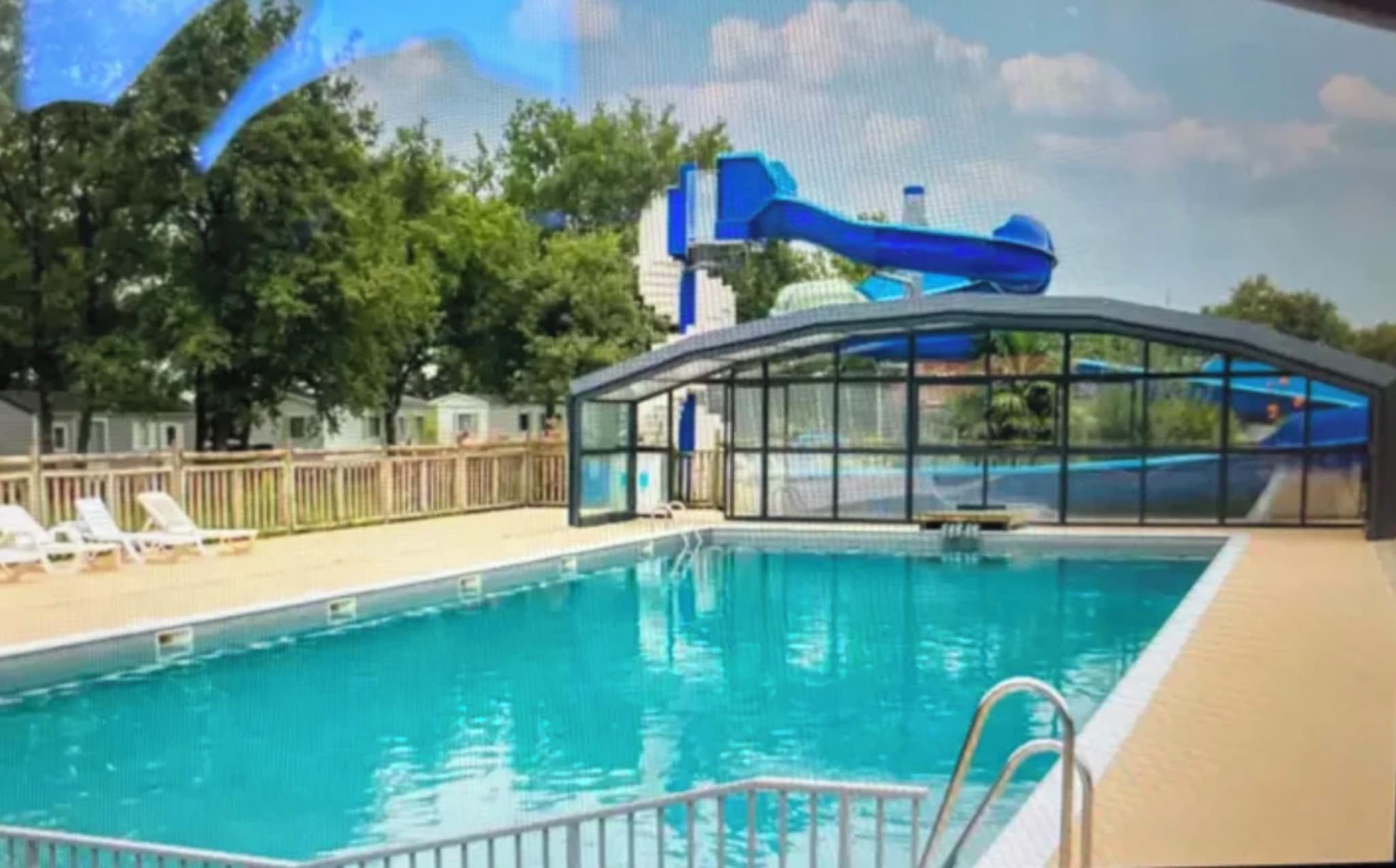 Ein Schwimmbad mit Wasserrutsche, Liegestühlen und einer überdachten Sitzgelegenheit.