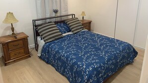 A bedroom with a bed, two bedside tables, a nightstand, a lamp, a drawer, a curtain, and a wardrobe.