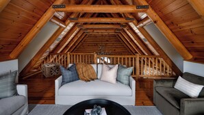 A cozy attic bedroom with a sloped ceiling, a bed with pillows, a coffee table, and a sofa.