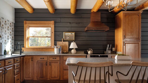 A kitchen with wooden cabinets, a window, a stove, and two bar stools.