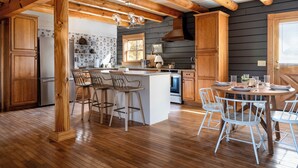 A spacious kitchen with wooden beams, a central island, bar stools, and a dining area with a round table and chairs.
