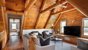 A log cabin interior with a loft bedroom, a living room with a TV, and a dining area.