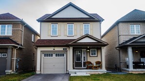 A two-story residential house with a garage, a front porch with a chair, and a small table.