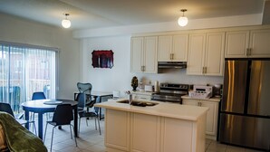 A modern kitchen with white cabinets, a stainless steel refrigerator, and a dining area with a round table and chairs.