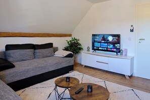 A modern living room with a grey sofa, a white cabinet, a television displaying a movie, and a small plant. - Charming half-timbered apartment with modern comfort, 110 sqm (Eltville am Rhein)