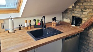 A kitchen with a wooden countertop, a black sink, and a dishwasher. There is a window above the sink, a brick wall, and a coffee maker on the counter. - Charming half-timbered apartment with modern comfort, 110 sqm (Eltville am Rhein)