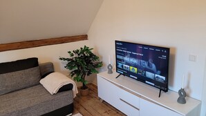 A modern living room with a flat-screen TV mounted on the wall, a grey sofa, a small potted plant, and a white cabinet. - Charming half-timbered apartment with modern comfort, 110 sqm (Eltville am Rhein)
