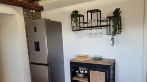 A kitchen with a stainless steel refrigerator, a wooden table with bowls, and a wall-mounted shelf with glassware and plants. - Charming half-timbered apartment with modern comfort, 110 sqm (Eltville am Rhein)