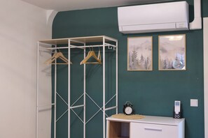 A room with a white wardrobe, a coat rack with wooden hangers, a small table with a clock, and two framed pictures on the wall. - Charming half-timbered apartment with modern comfort, 110 sqm (Eltville am Rhein)