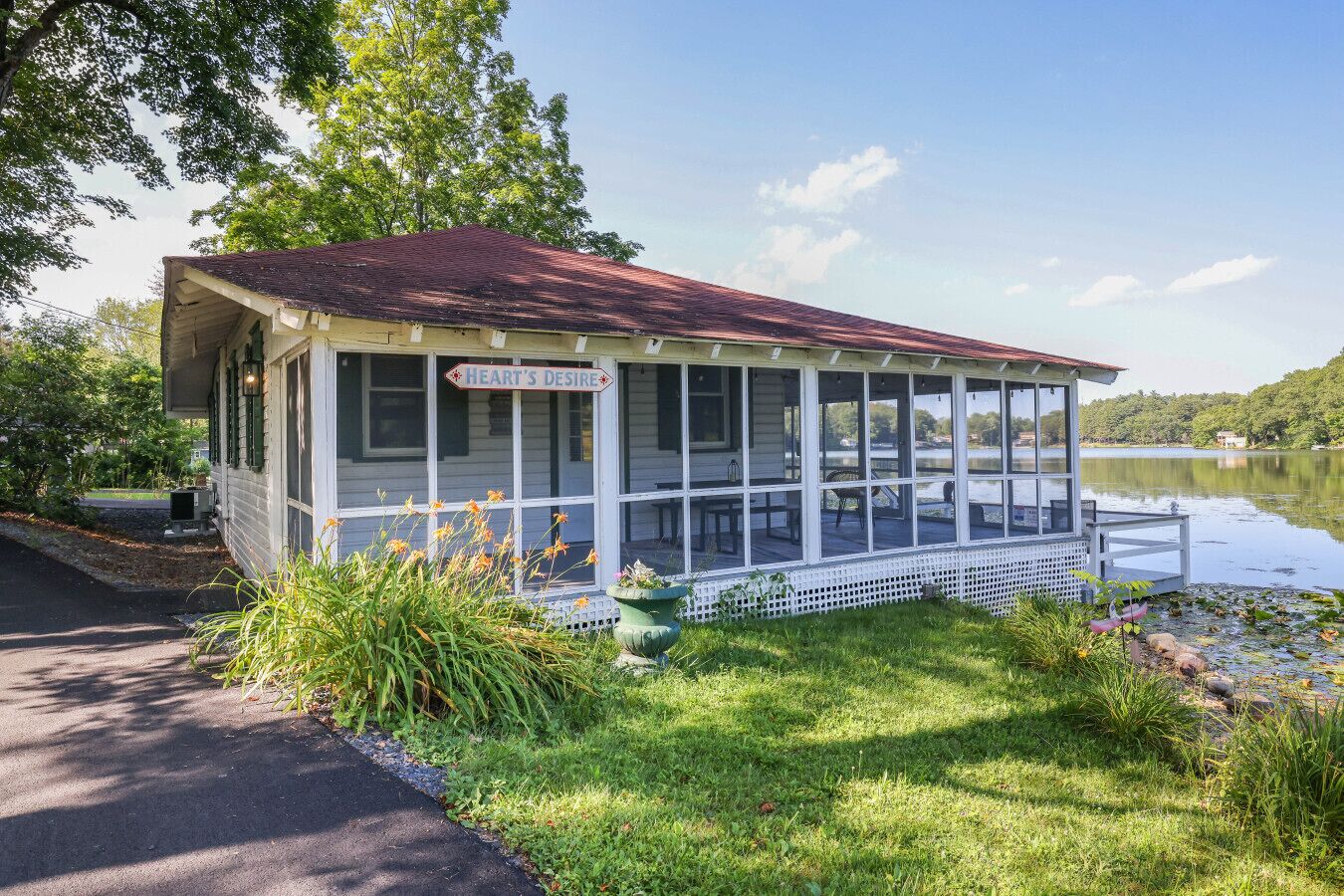 A covered dock with a sign reading "Heart's Desire," surrounded by lush greenery and a calm lake.