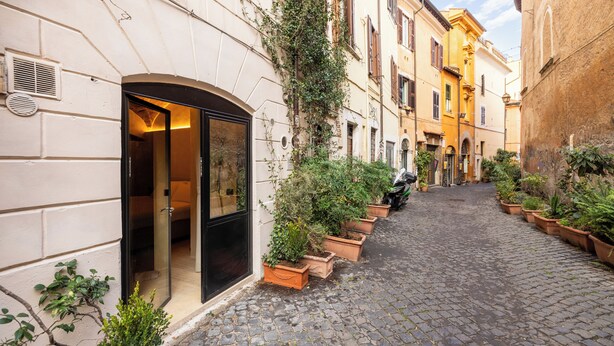 Una estrecha calle adoquinada flanqueada por macetas de terracota y una hilera de edificios con ventanas y puertas de arco.