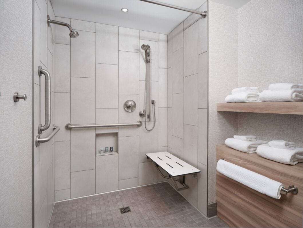 Un baño moderno con ducha, barras de apoyo, un banco y un perchero para toallas.