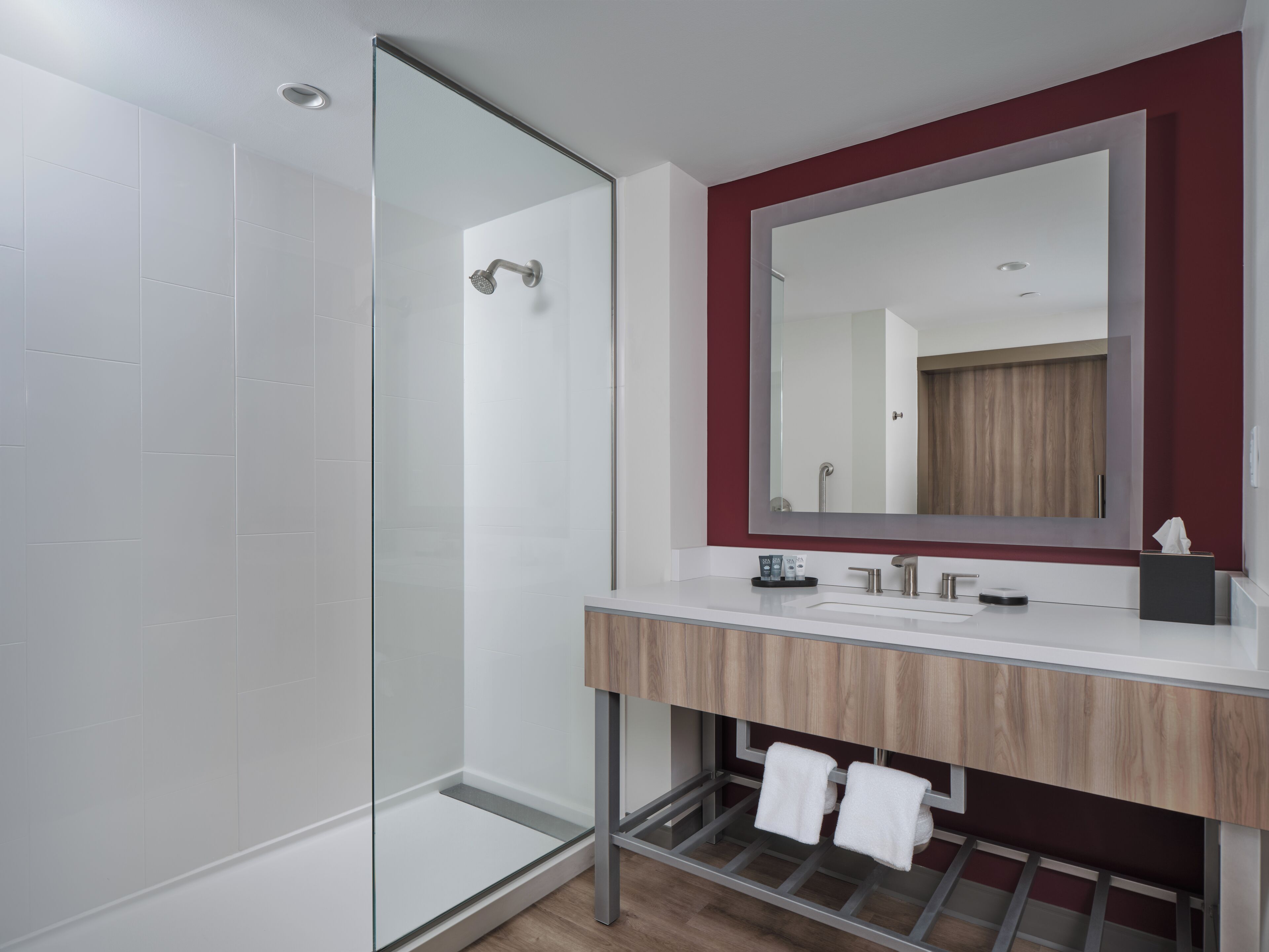 A modern bathroom with a glass shower enclosure, a wooden vanity with a mirror, and a towel rack.