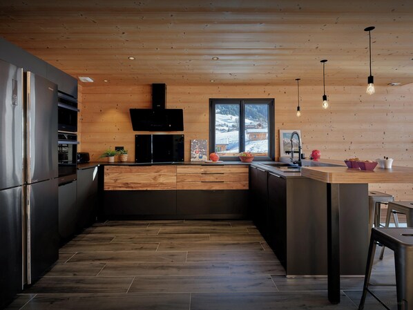 Una cocina moderna con techo de madera, electrodomésticos de acero inoxidable y un amplio ventanal con vistas nevadas.