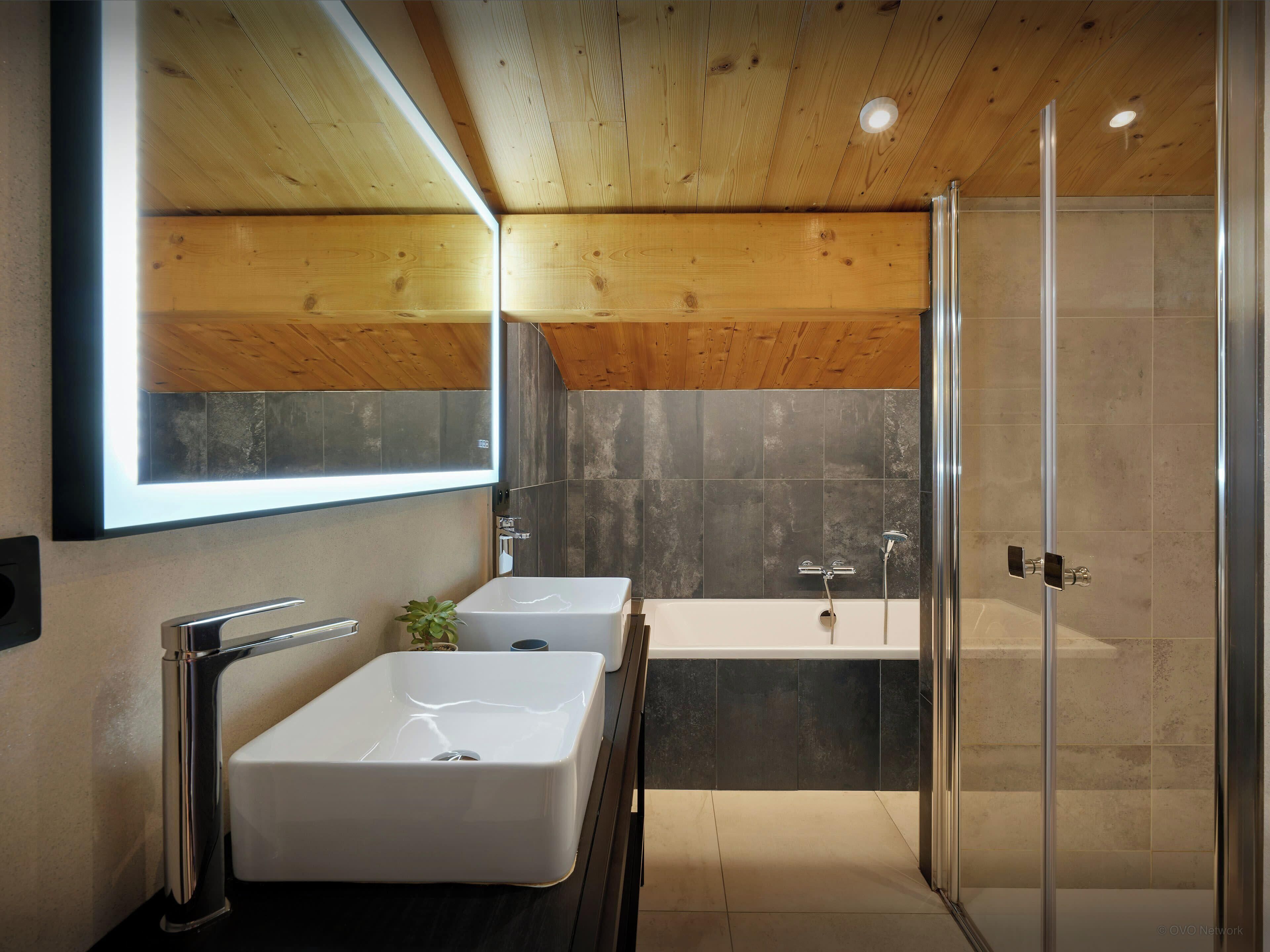 Un baño moderno con dos lavamanos, un espejo grande y cabina de ducha con paredes de vidrio.