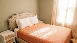 Ein ordentlich bezogenes Bett mit einer orangefarbenen, gemusterten Tagesdecke, weißen Kissen und einem Kopfstück mit einer gepolsterten Optik.