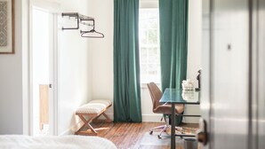A bedroom with a bed, a desk, a chair, and a window with curtains. - The Darlington Room @ Main Street Lofts (Victoria)