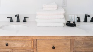 A bathroom with two sinks, a mirror, and a stack of white towels. - The Victorian Room @ Main Street Lofts (Victoria)