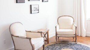 A room with a round rug, two chairs, a small table, and a hanging light fixture. - The Victorian Room @ Main Street Lofts (Victoria)