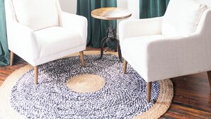 A room with two white armchairs, a round wooden table, and a large window with green curtains. - The Scotsman Room @ Main Street Lofts (Victoria)