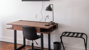 A minimalist office setup with a wooden desk, a black office chair, a black desk lamp, and a black metal bench. - The Scotsman Room @ Main Street Lofts (Victoria)