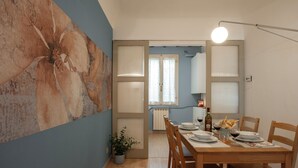 A dining area with a wooden table set for two, a potted plant, and a bottle of wine. - Ricasoli 37 - Flo Apartments (Firenze)