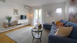 A modern living room with a blue sofa, a glass coffee table, a white entertainment unit, and a large window with curtains. - Ricasoli 37 - Flo Apartments (Firenze)