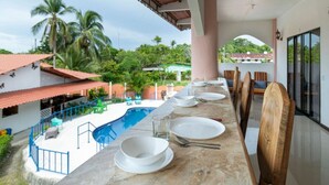 Ein Esszimmer mit Geschirr und Besteck, mit Blick auf einen Swimmingpool und üppiges Grün.