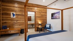 Une chambre d’hôtel avec un mur en bois, un lit, un bureau, une chaise, une petite table avec une lampe et un tableau accroché au mur.