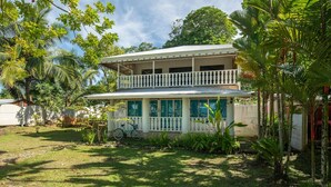 A two-story house with a balcony, surrounded by lush greenery and a bicycle. - Gardenview Retreat | Beachfront | Walk Everywhere (Manzanillo)