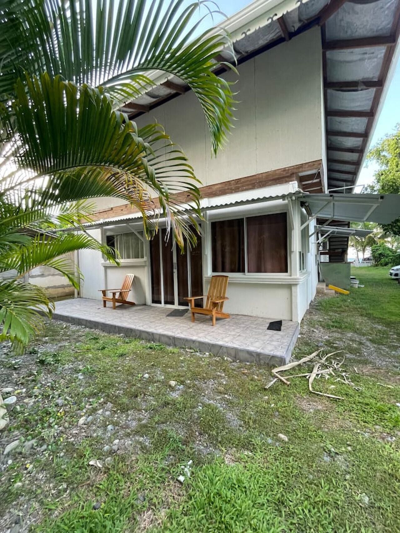 Ein Haus mit verdeckter Veranda, zwei Holzstühlen und einer Palme.
